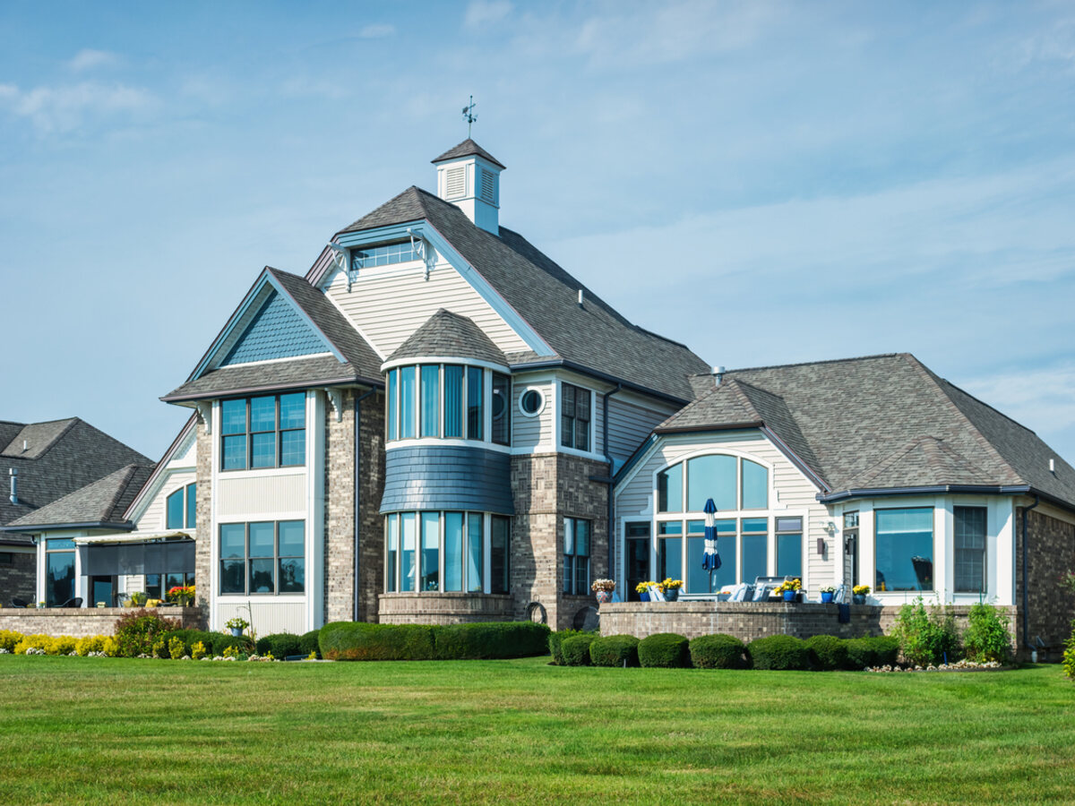 A large lakeside home with abundant tall windows and a manicured lawn under a Midwest summer sky.